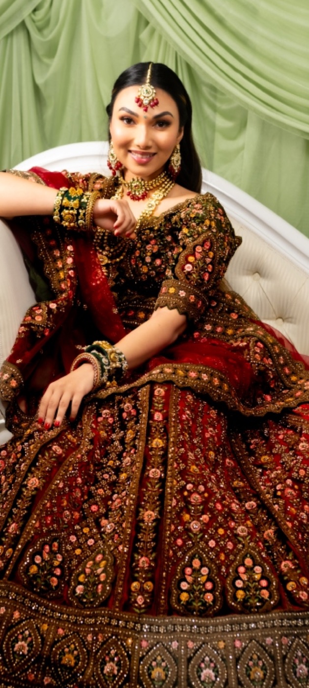 Bride in a red and gold lehenga seated on an ivory chaise