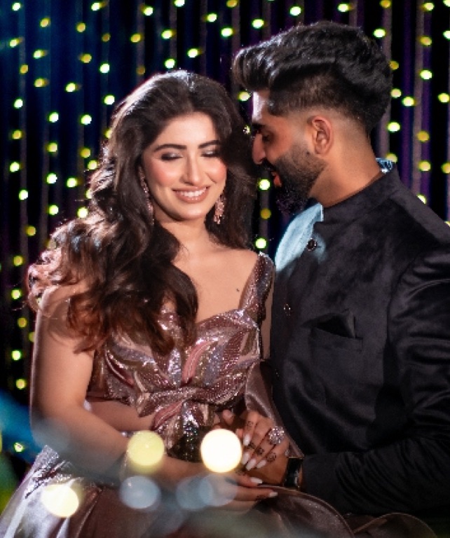 Couple in evening wear smiling at each other, lights glowing behind them