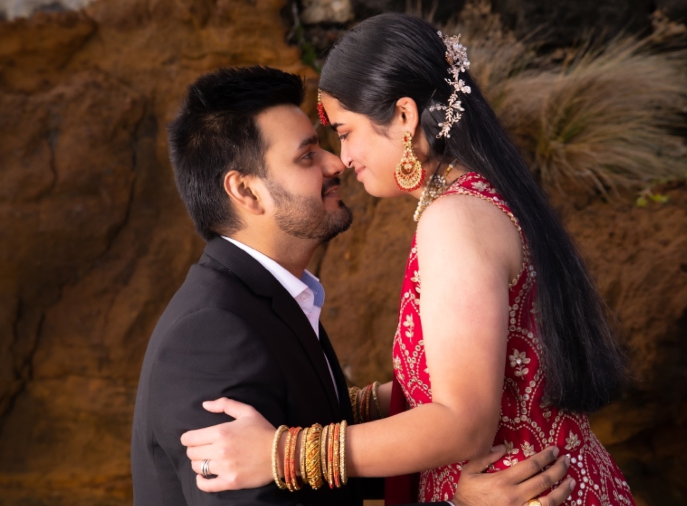 Couple leaning in, foreheads almost touching, beside a sandstone cliff