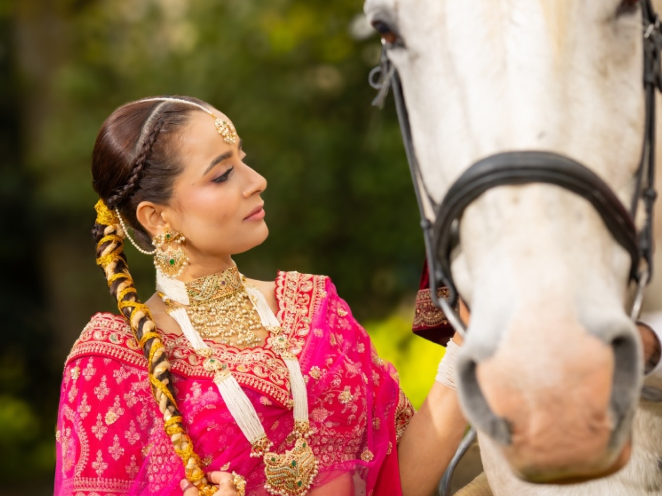 Bride in pink and gold standing beside a white horse