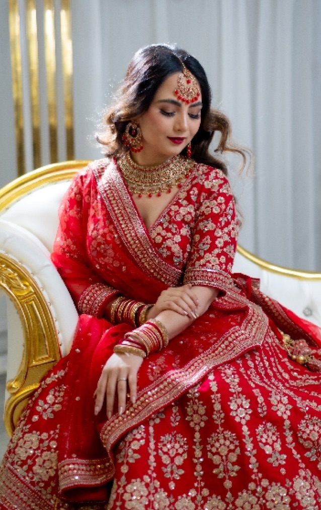 Bride in a red lehenga seated on a gold-trimmed chair