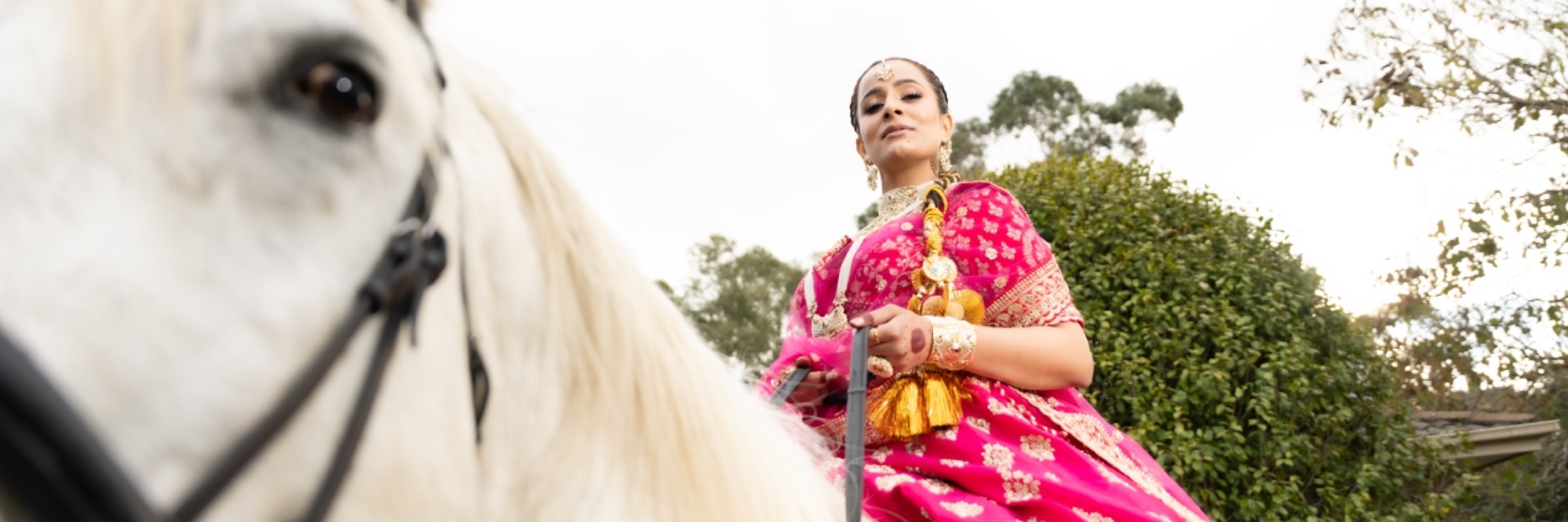 Bride in a pink lehenga on horseback, with a white horse in the foreground